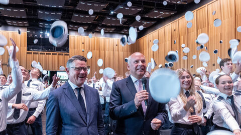 Angehende Polizeibeamtinnen und-beamte werfen ihre Mützen in die Luft, im Vo