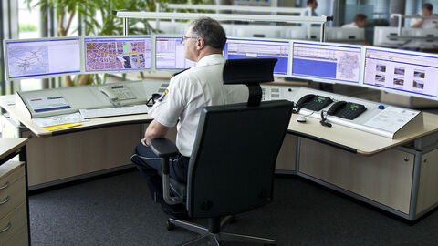 Ein Polizist sitzt an einem halbrunden Schreibtisch, vor ihm mehrere Monitore.