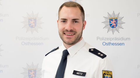 Eine Kollege in weißem Uniformhemd vor der Medienwand mit dem Aufdruck Polizeipräsidium Osthessen