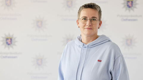 Eine Kollegin mit Pullover und Brille vor der Medienwand mit dem Aufdruck Polizeipräsidium Osthessen