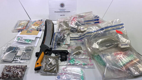 Sichergestellte Gegenstände der OE City; Foto zeigt die auf einem Tisch abgelegten und in durchsichtige Tüten verpackten Gegenstände sowie eine schwarze Pistole und eine im Schaft steckende Machete