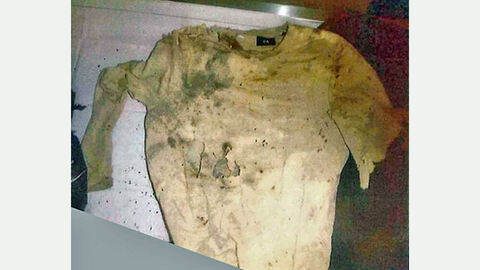 Oberteil des unbekannten Toten: Zerrissenes Oberbekleidungsstück in weiß mit Schmutzanhaftungen auf einem Tisch liegend