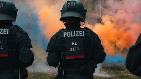 Zwei Einsatzkräfte von hinten mit orangener Rauchwolke im Hintergrund 