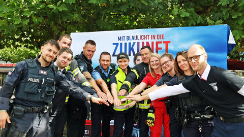 Veranstaltung "Respekt zeigen - Respekt erfahren: Begegnungen mit der Blaulichtfamilie"; Mehrere Personen in verschiedenen Uniformen stehen im Halbkreis und strecken die Hände nach vorne