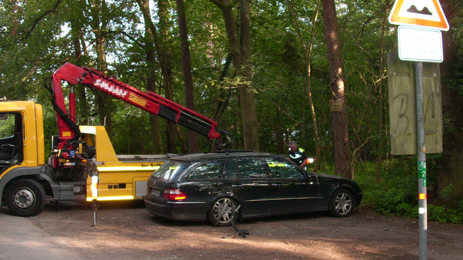 Ein schwarzer Mercedes Kombi auf einem Waldparkplatz, dahinter ist ein Abschleppwagen zu sehen